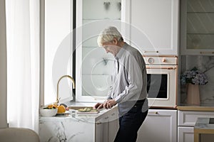 Older retired homeowner man cooking salad in modern kitchen