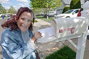 Older senior citizen woman smiles as she removes a blank white envelope from a white mailbox