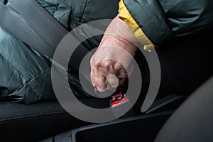 Older senior woman fastens a safety belt in a car wearing green and yellow jacket