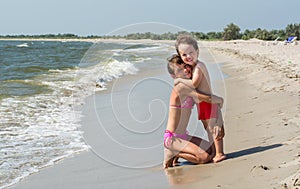 The older sister hugs her younger brother on the beach with waves and sea foam, happy children.