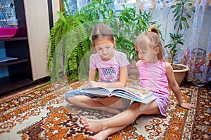 The older sister is reading a big book with fairy tales to her younger sister. Children play together at home