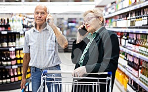 Older spouses talking on the phone in supermarket