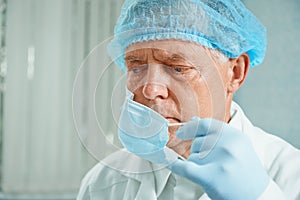 Older surgeon takes off his protective mask