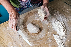 Older woman baker cutting dough in home kitchen