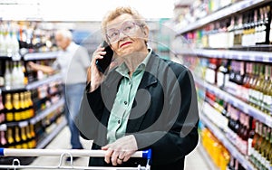 Older woman with glasses talking on the phone in the supermarket