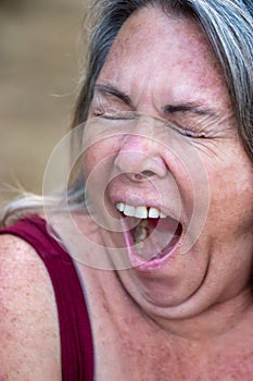 Older woman with gray hair and age spots yawning outside