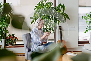 Older woman with headphones on head, listening music, relaxing at home.