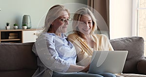 Older woman her young daughter sit on sofa with laptop