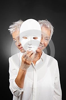 Older woman hiding happy and sad face behind mask photo