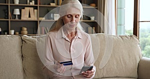 Older woman holds cellphone and credit card buying on internet