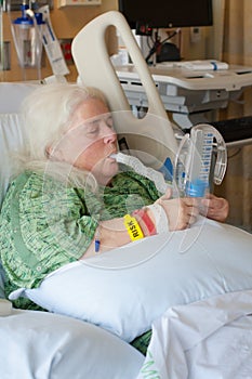 Older woman in hospital bed using incentive spirometer