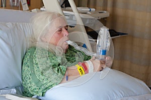 Older woman in hospital bed using incentive spirometer photo