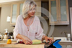 Older woman in kitchen searching for recipe on digital tablet