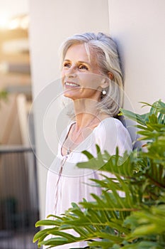 Older woman leaning on wall outside smiling