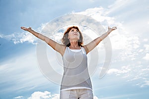 Older woman opening up her arms to exercise yoga outdoors