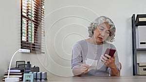 older woman paying bills using a smart phone at home