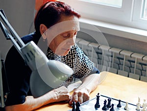 An older woman plays chess with her grandson. Joint family games at home.