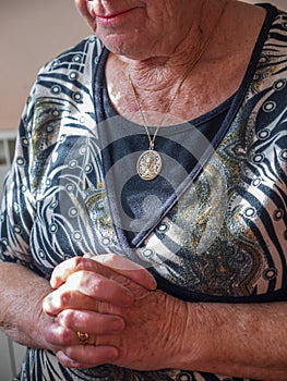 Older woman praying with linked hands and a gold medallion with the Virgin