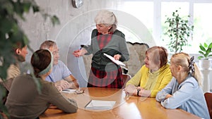 Older woman presides over support group meeting with mature people listening