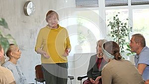 Older woman presides over support group meeting with mature people listening