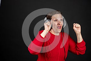 Older woman with a set of retro corded headphones in a red sweater dancing and enjoying music