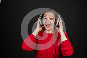 Older woman with a set of retro corded headphones in a red sweater dancing and enjoying music.