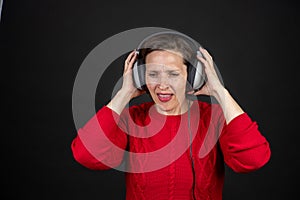 Older woman with a set of retro corded headphones in a red sweater dancing and enjoying music.