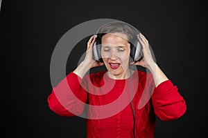 Older woman with a set of retro corded headphones in a red sweater dancing and enjoying music.