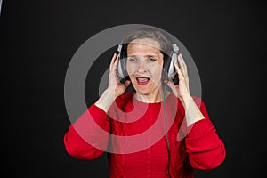 Older woman with a set of retro corded headphones in a red sweater dancing and enjoying music.