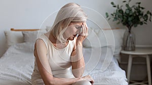 Older woman sit on bed coping with morning headache concept