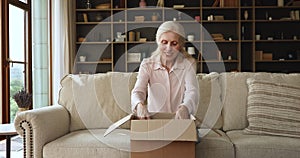 Older woman sit on couch unpack parcel box with books