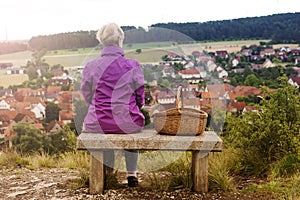 Older woman sitting on bench and looking at small town