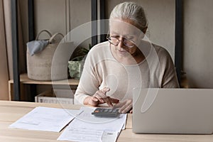 Older woman sitting at table using calculator manage personal budget