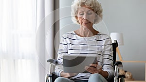 Older woman sitting in wheelchair, using computer tablet