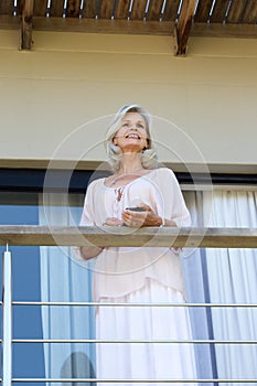 Older woman smiling and standing on balcony with smart phone