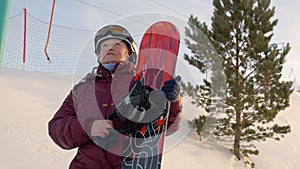 Older woman standing with snowboard at mountains.