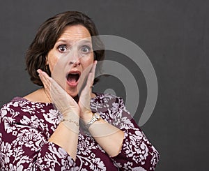 Older woman in the studio with a look of surprise holding hands to face with open mouth