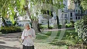 Older woman text mobile phone in summer park. Stylish short hair senior browse