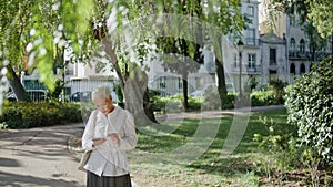 Older woman text mobile phone in summer park. Stylish short hair senior browse photo