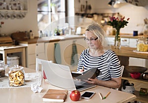 Older woman working from homeoffice. The retiree earning extra money during retirement. Woman paying bills online.