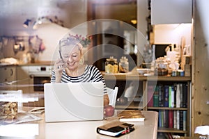 Older woman working from homeoffice, typing on laptop, making phone calls. The retiree earning extra money during