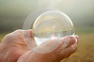 Older womans hand holding a shiny glass sphere