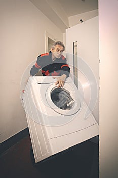 Older worker trasporting wash machine appliace with cart to elevator