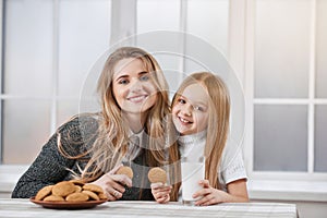 Older and younger sisters eating cookies and smile.