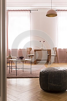 Oldschool leather pouf in stylish living room interior with two coffee table and pastel pink carpet on parquet floor