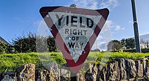 Oldy yield sign Ireland on Irish road with green grass, stone