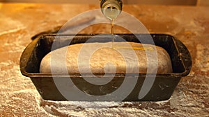 Olive oil being poured over dough in loaf tin on a floury table