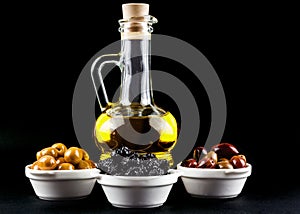 Olive oil bottle and olives in bowls on black.