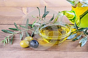 Olive oil dripping in the glass transparent bowl. Fresh olives, branches of olive tree on the wooden background