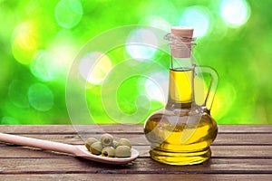 Olive oil extra virgin in the bottle and olives on wooden spoon. Wooden table and green bokeh background